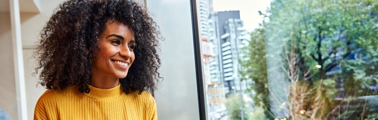 Smiling African-American woman holding coffee cup and looking out window