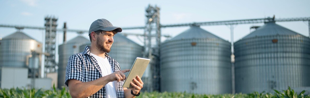 Farmer using tablet in front of grain elevators