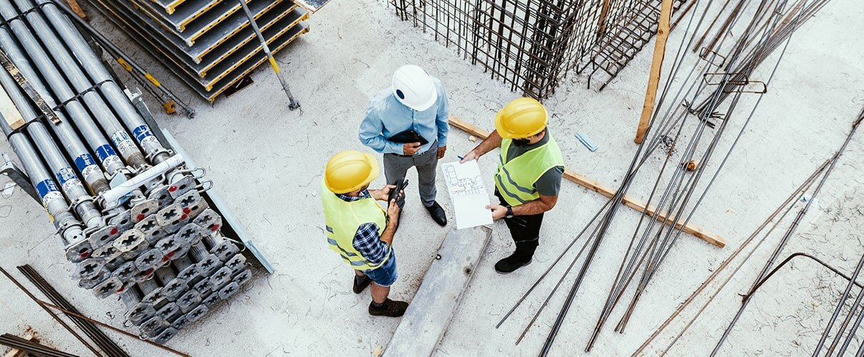 Three workers in hard hats reviewing blueprints at construction site
