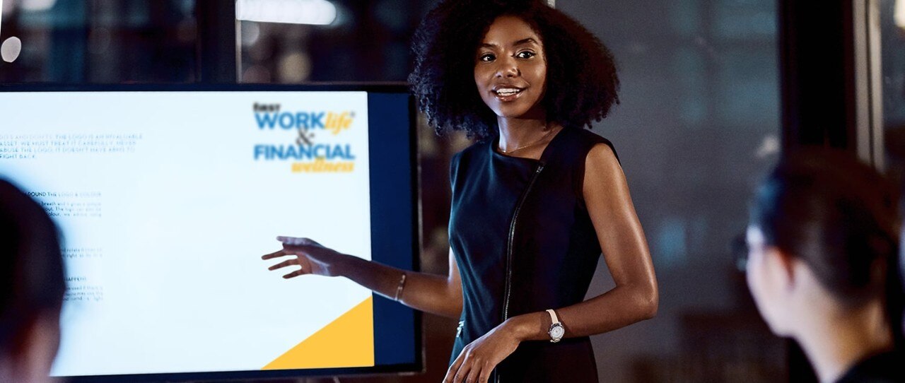 Female banker presenting in front of video screen with First WORKlife® and Financial Wellness logo