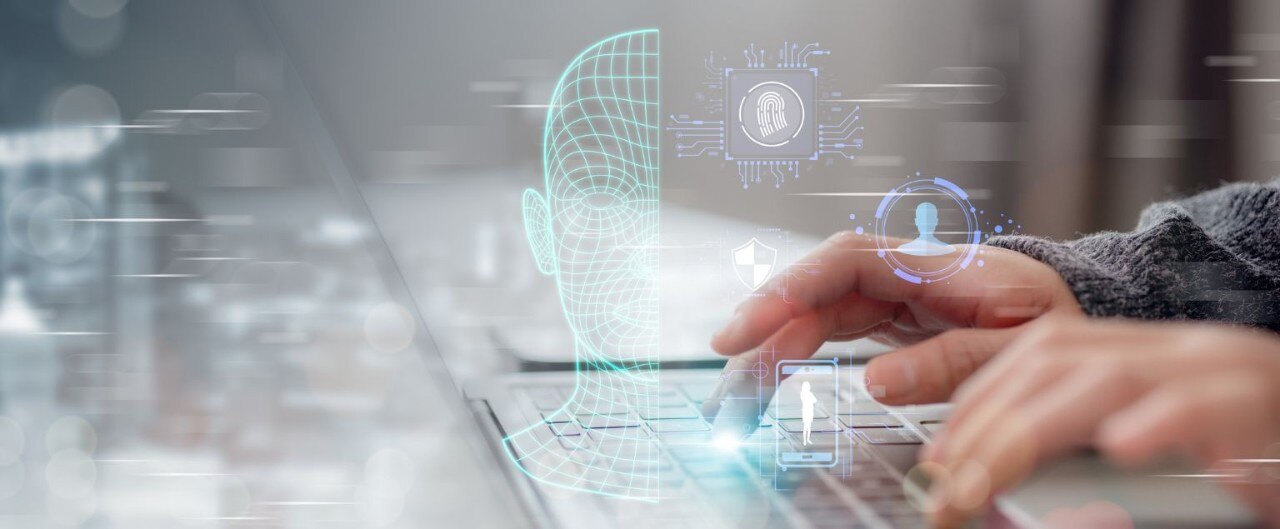 Hands typing on a laptop, with superimposed graphics of facial scans and fingerprints