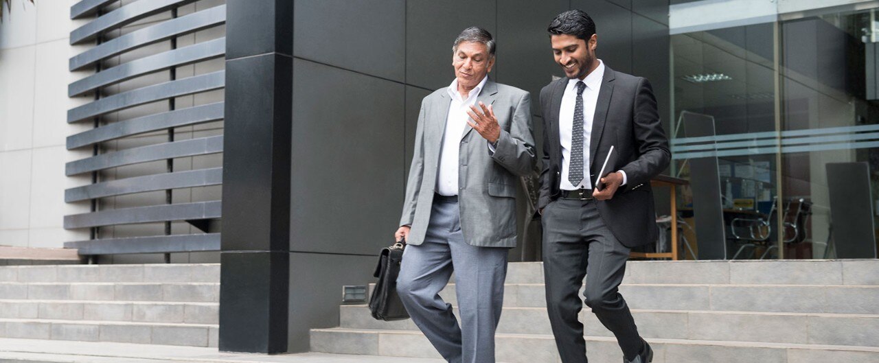 Older businessman talking with younger colleague as they leave the office