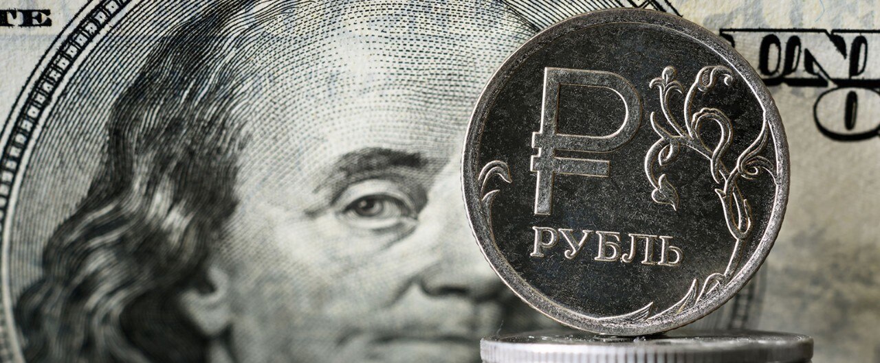 Russian Ruble coins with an American $100 bill in the background