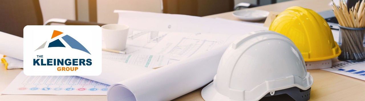 A desk with hard hats, blueprints, and pencils. Overlay of a logo, “The Kleingers Group.”