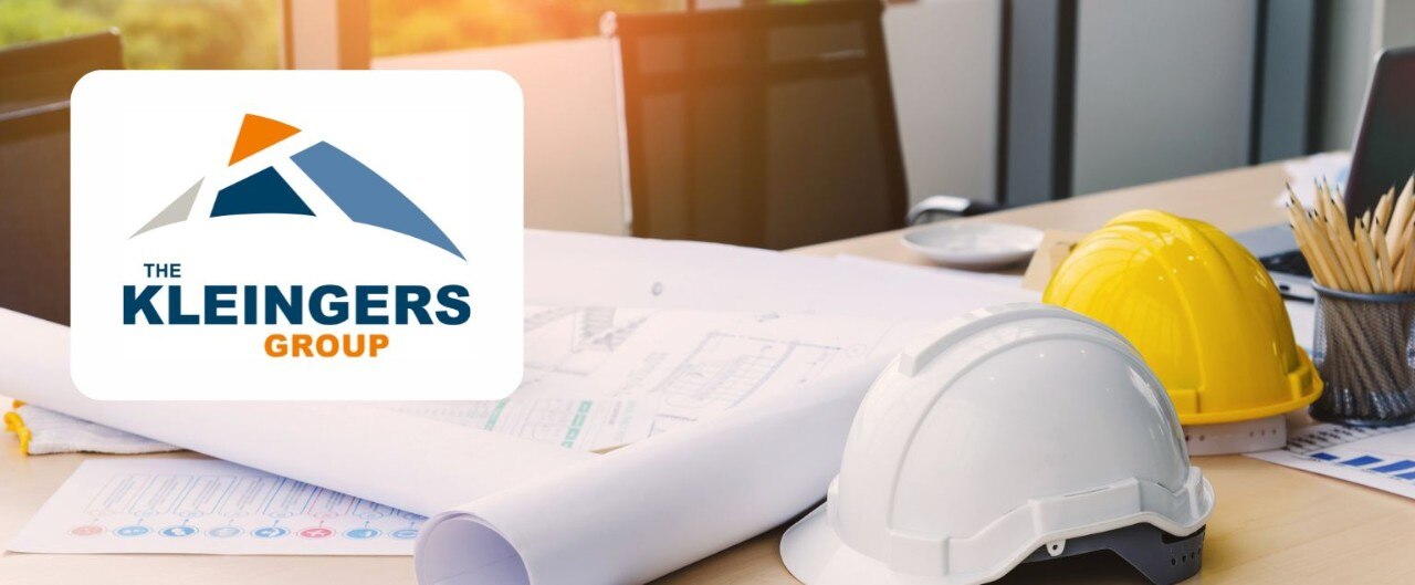 A desk with hard hats, blueprints, and pencils. Overlay of a logo, “The Kleingers Group.”