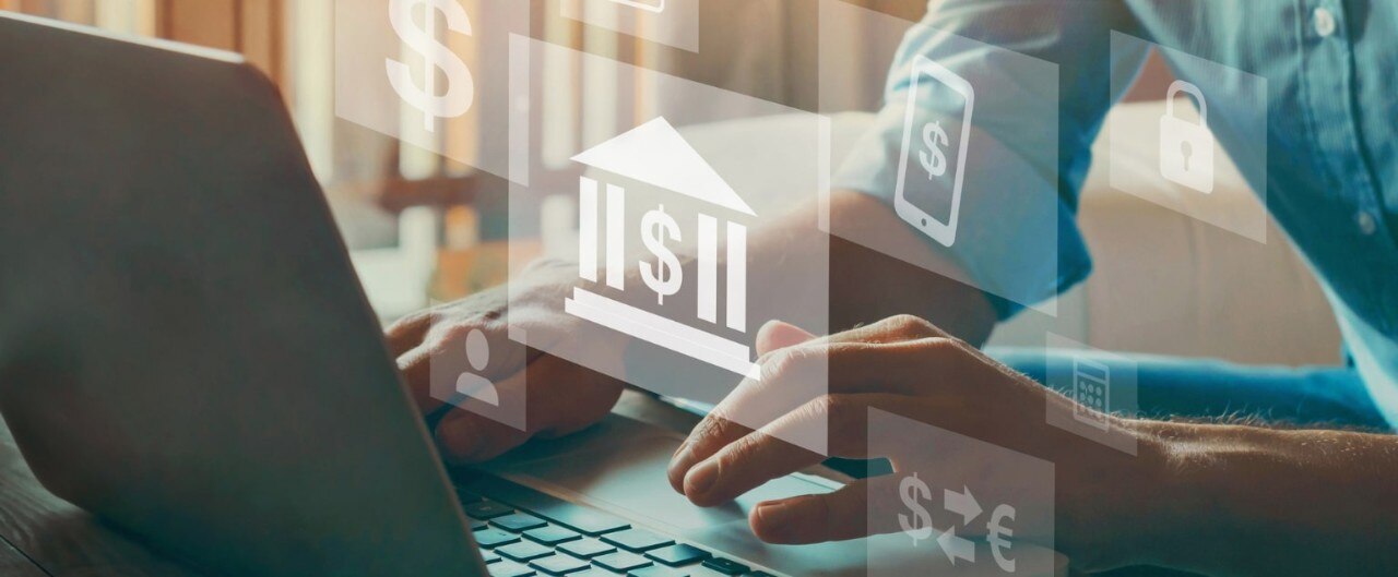 Hands working at laptop with superimposed financial icons floating in the air