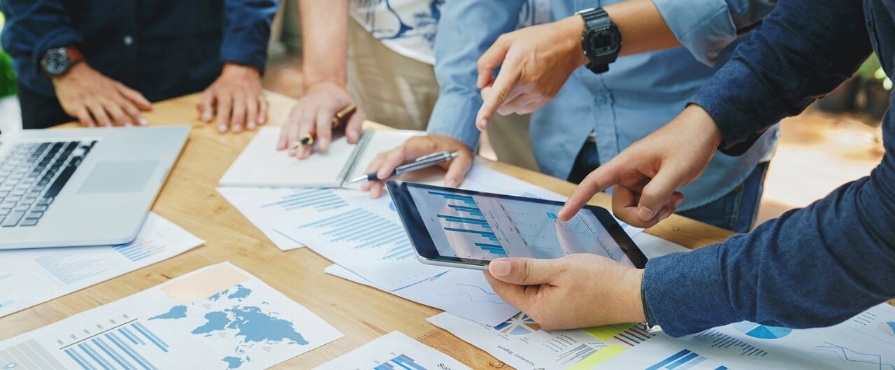 A group of people around a table with charts and graphs and a tablet