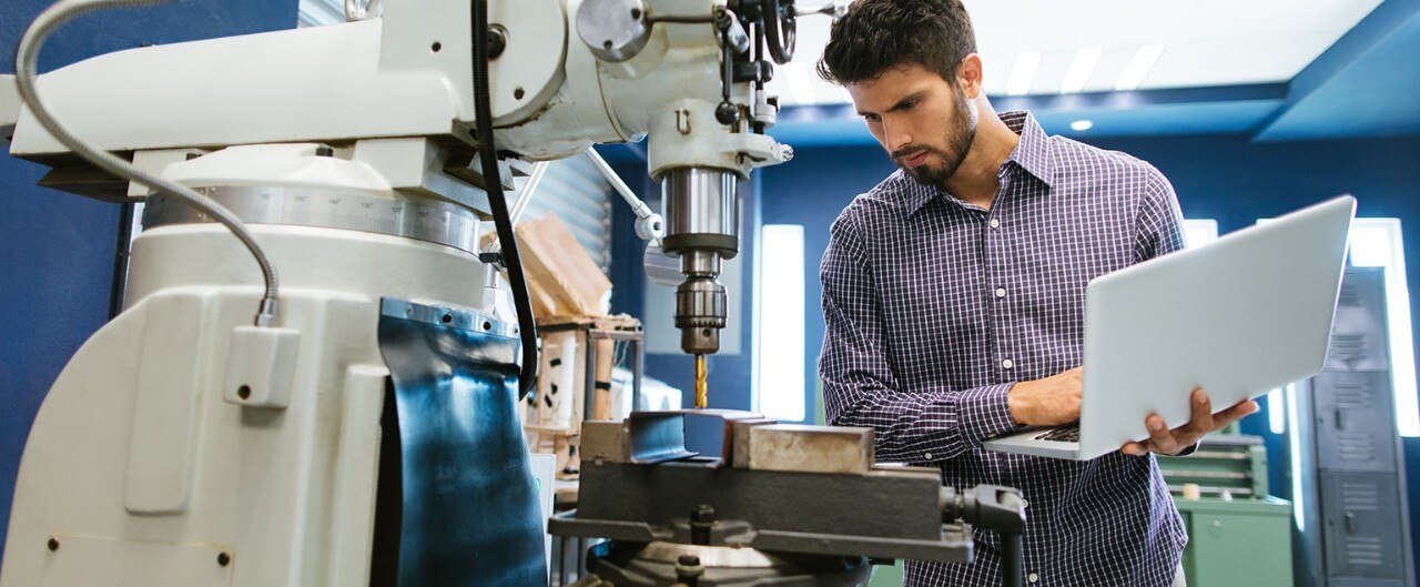 A man with a laptop looks over machinery