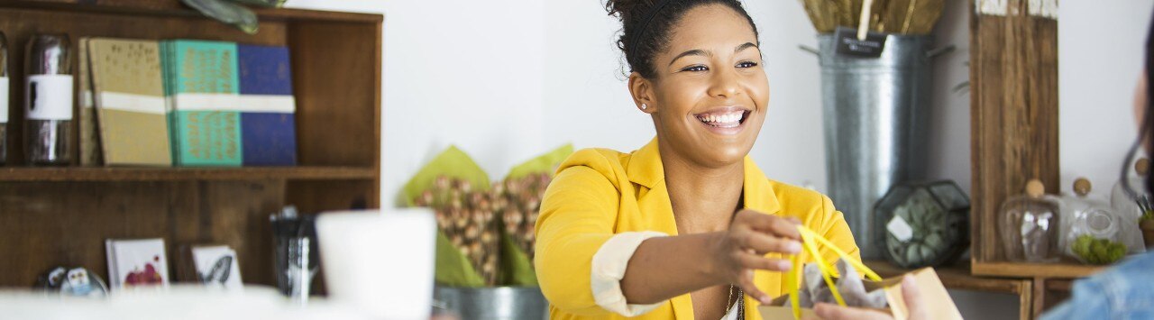Friendly African-American boutique owner handing customer a gift bag
