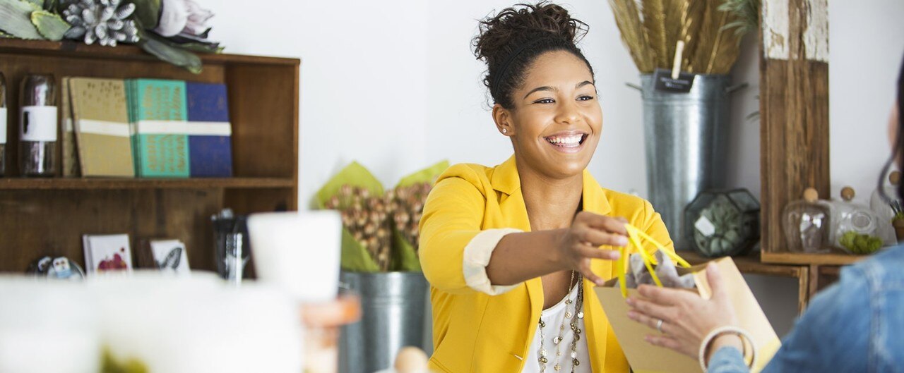 Friendly African-American boutique owner handing customer a gift bag