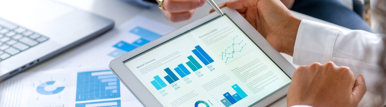 Close-up of people's hands as they review financial data on a tablet and paper documents