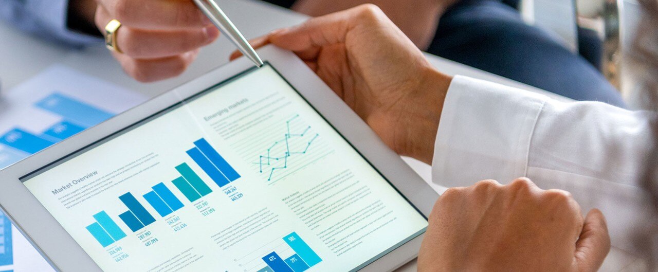 Close-up of people's hands as they review financial data on a tablet and paper documents