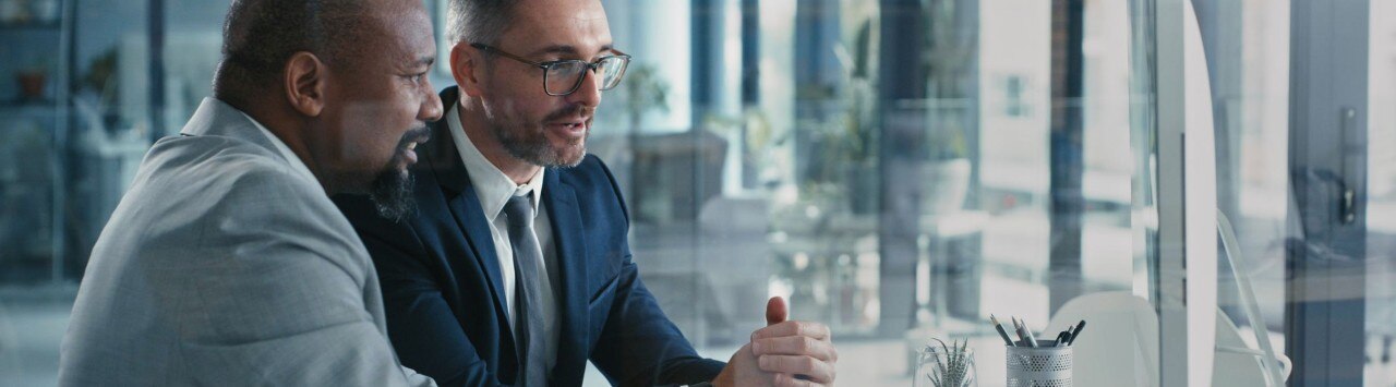 Two businessmen wearing suits, in discussion, facing a laptop in an office