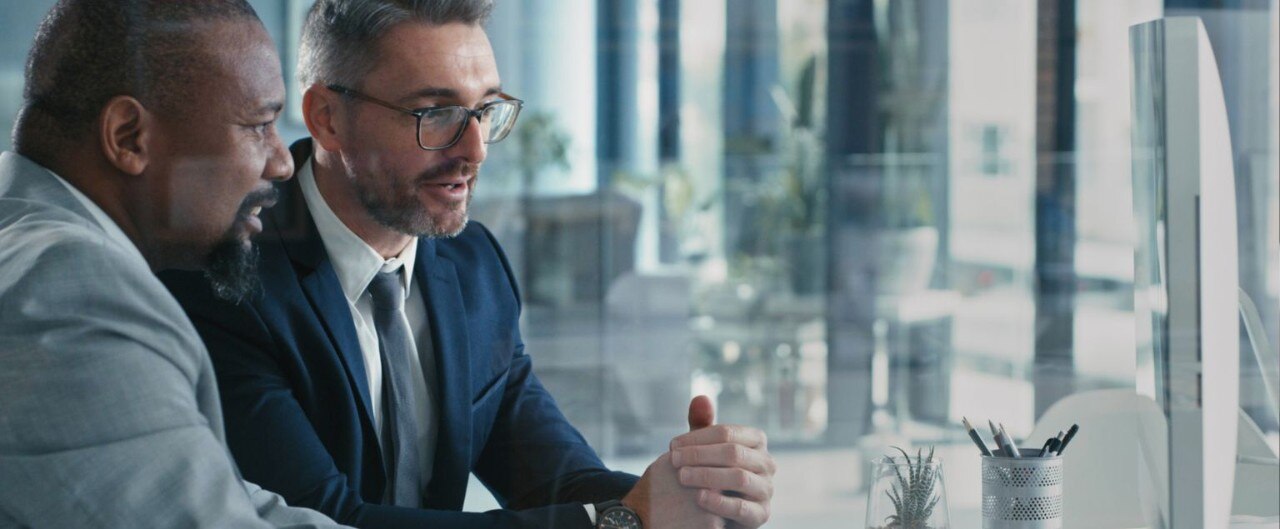 Two businessmen wearing suits, in discussion, facing a laptop in an office