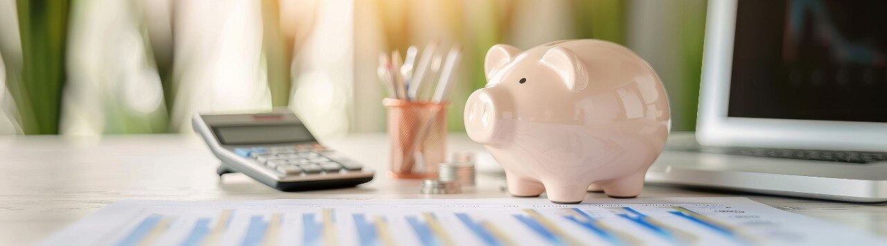 Desk with financial paperwork, calculator, pencil jar, stacks of coins and pale pink piggy bank.