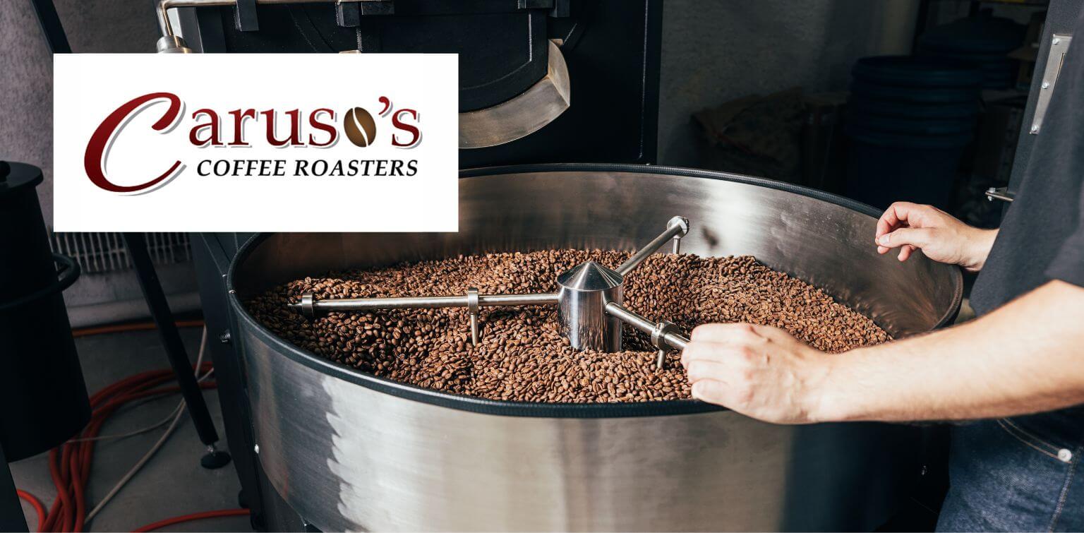 A person observes coffee beans roasting in high-capacity drum with Caruso's Coffee Roasters logo