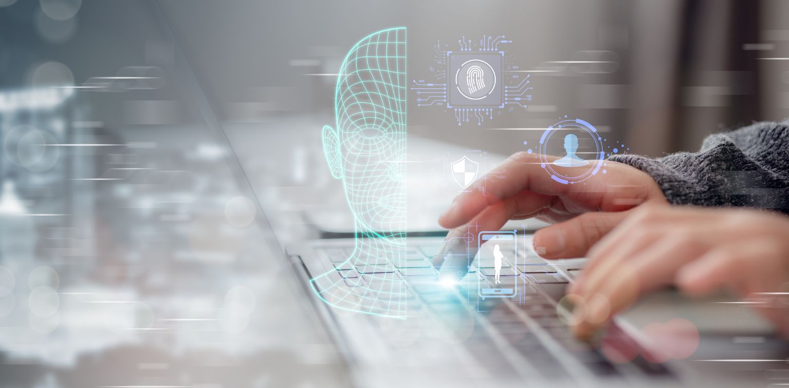Hands typing on a laptop, with superimposed graphics of facial scans and fingerprints