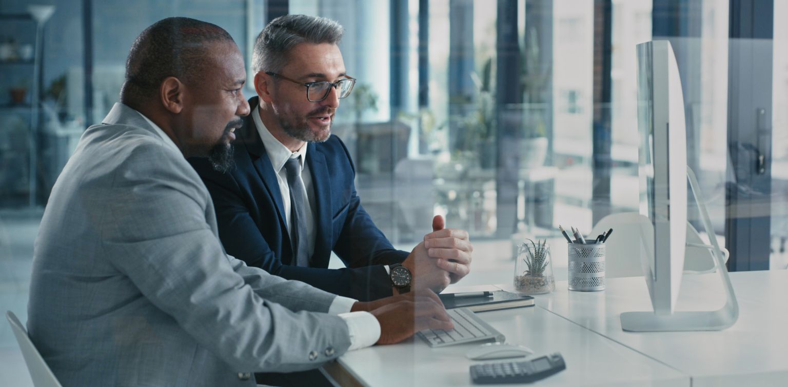 Two businessmen wearing suits, in discussion, facing a laptop in an office