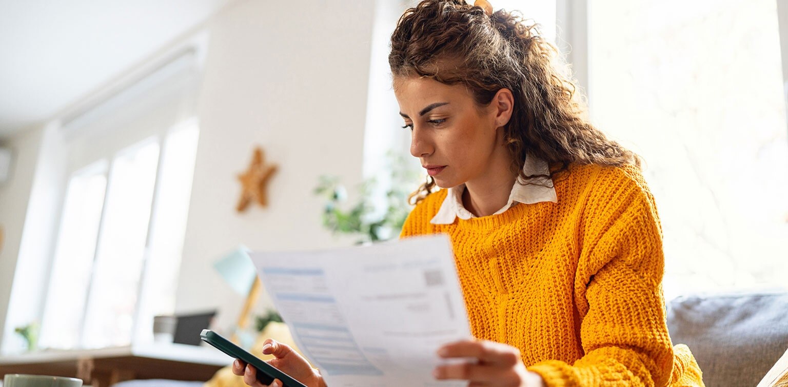 Caucasian woman reviewing financial document and holding smartphone