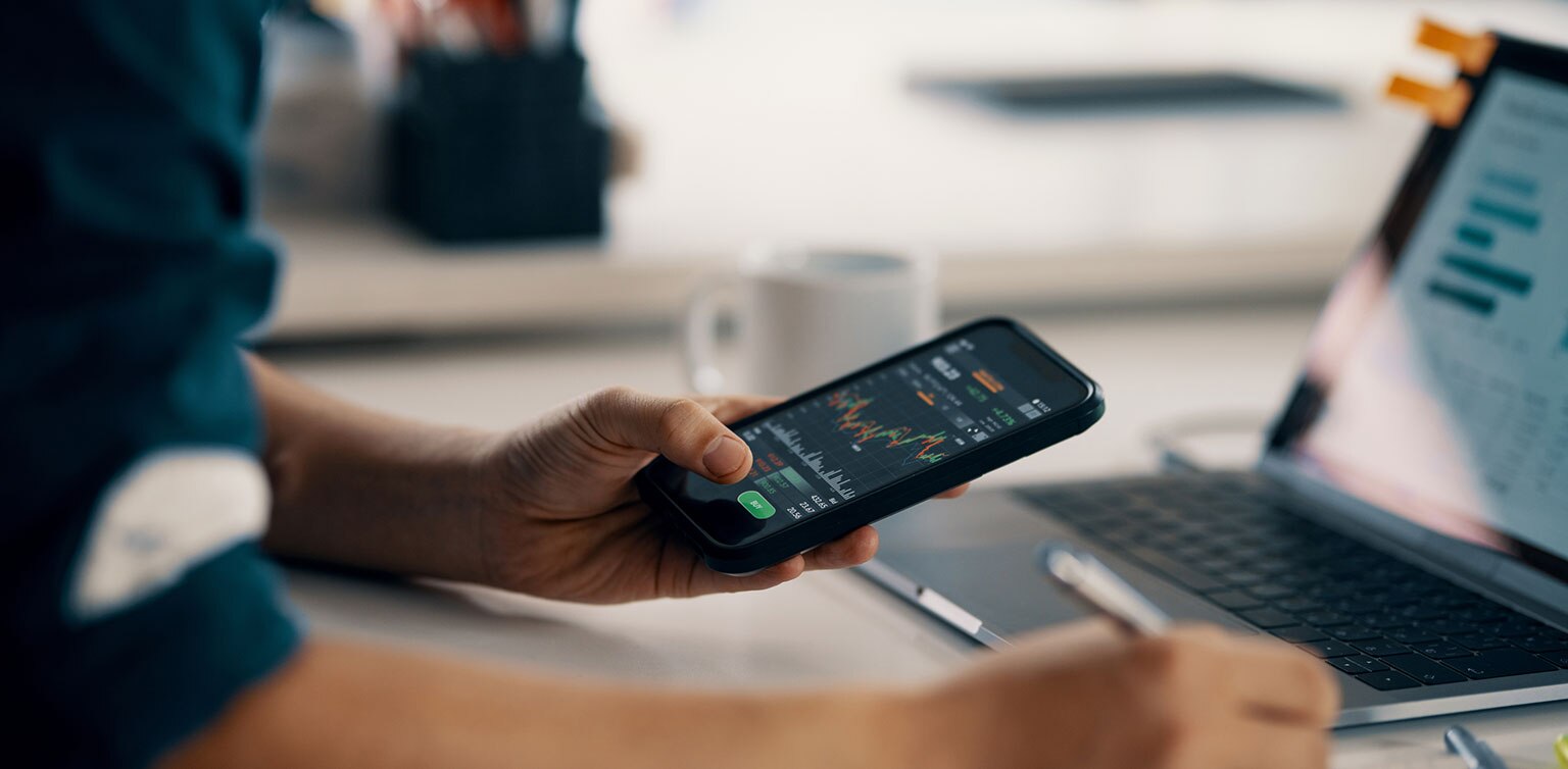 Man reviewing financial data on smartphone and laptop