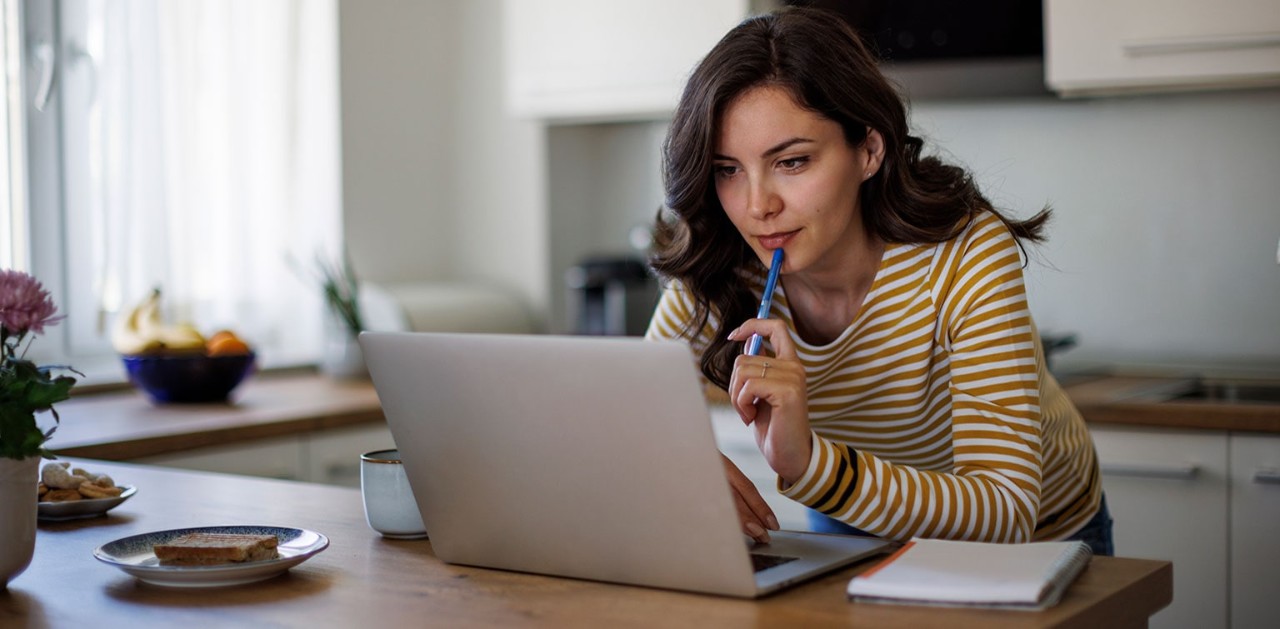 Young woman working on laptop while eating breakfast