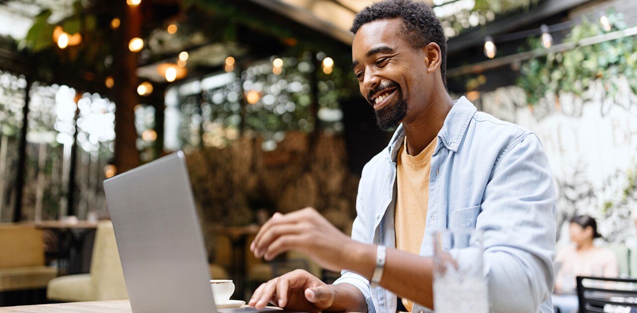 Smiling African-American man using laptop at outdoor cafe 