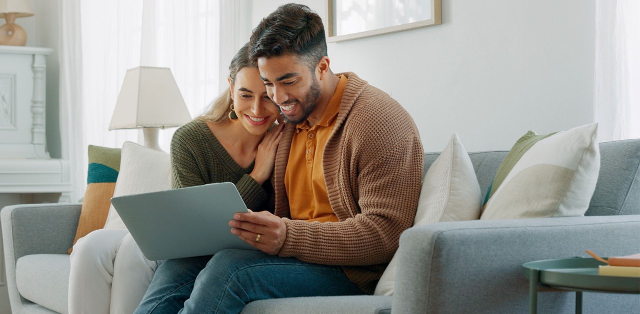 Young smiling Hispanic couple looking at laptop on sofa