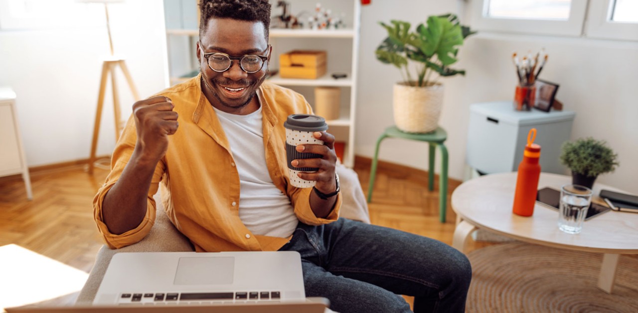 Cheerful African-American male college student holding coffee and looking at laptop
