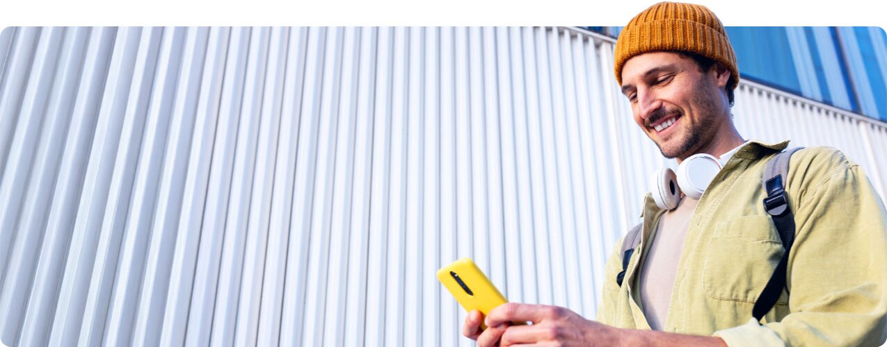 Young man wearing beanie and headphones smiling and looking at smartphone