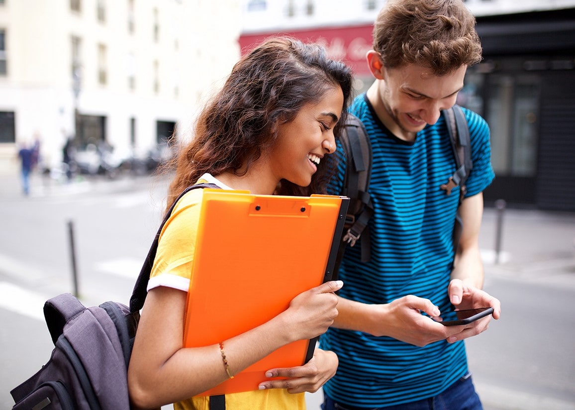 Smiling female and male student walking and looking at smartphone