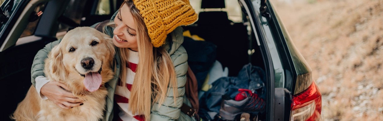 Woman hugging golden retriever sitting in the back of SUV