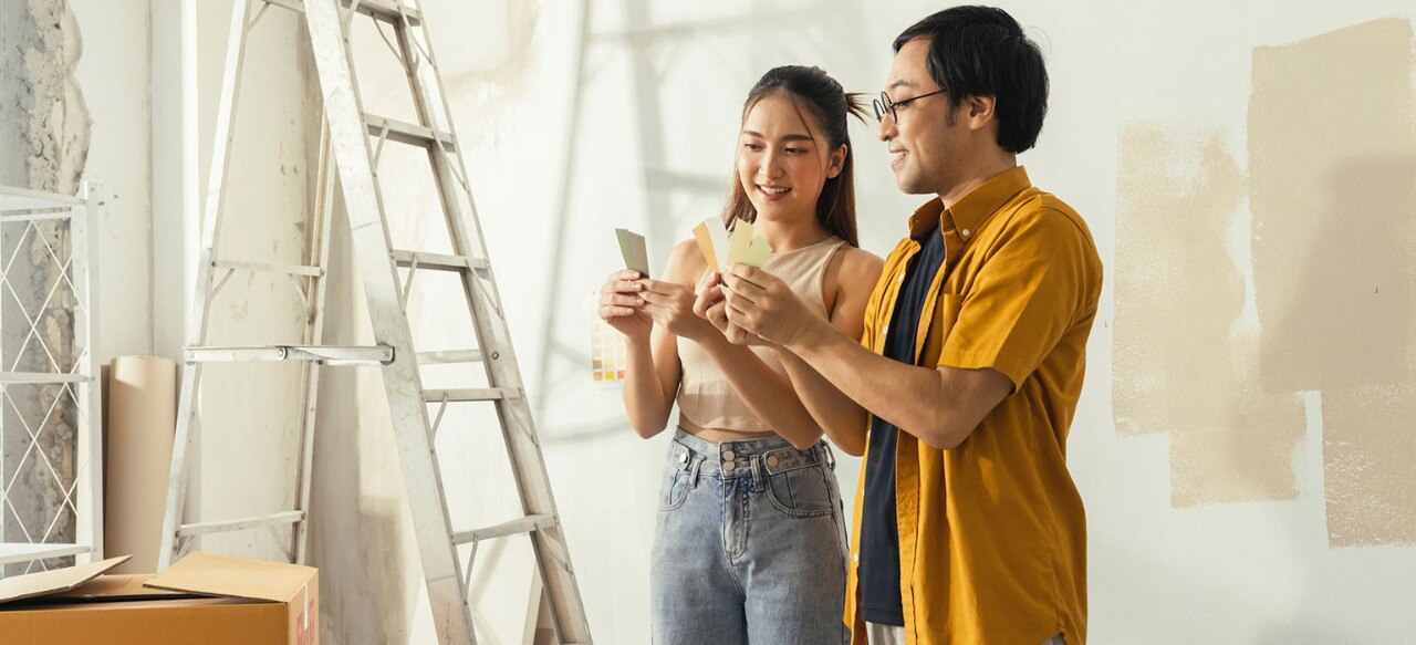 Smiling Asian couple comparing paint swatches in a room being renovated