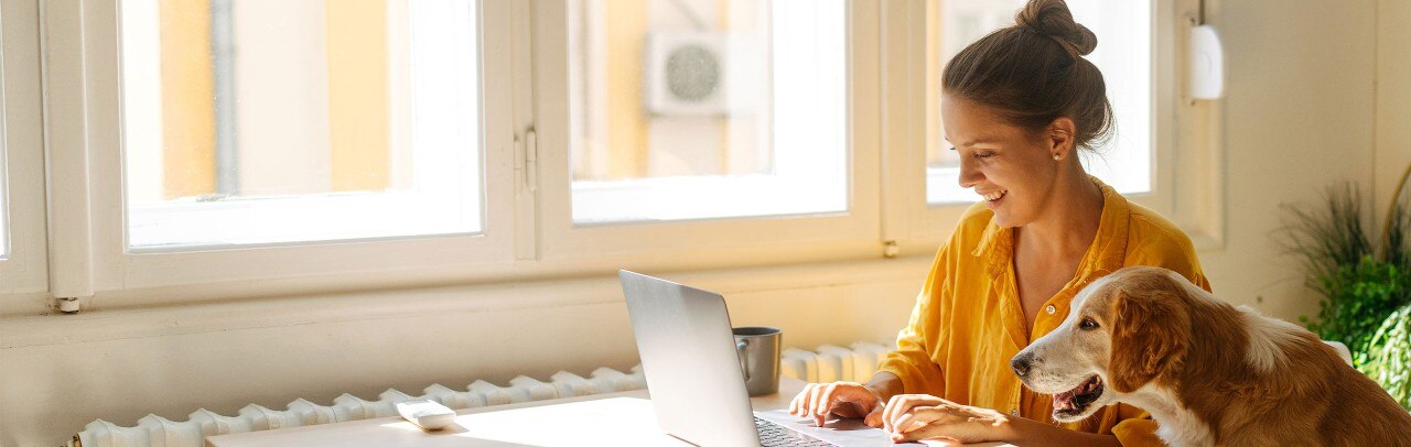Young Caucasian woman smiling and working on laptop while her dog looks on