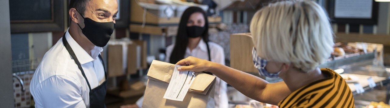 Masked deli employee handing carryout bag to customer