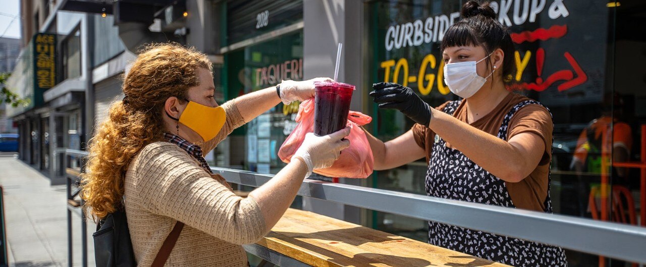Masked restaurant employee hands order to customer at curbside pick-up