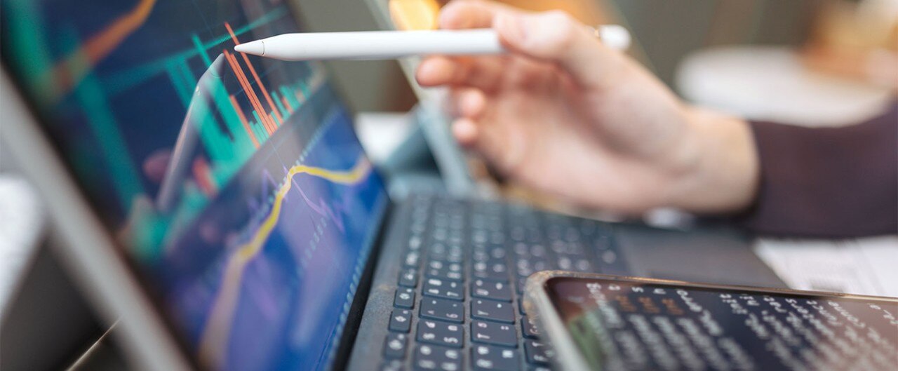 Person pointing a stylus at a digital display of financial data