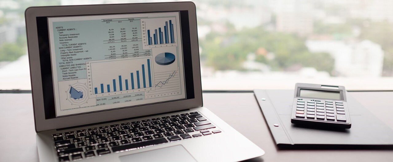 Open laptop displaying financial data, next to calculator