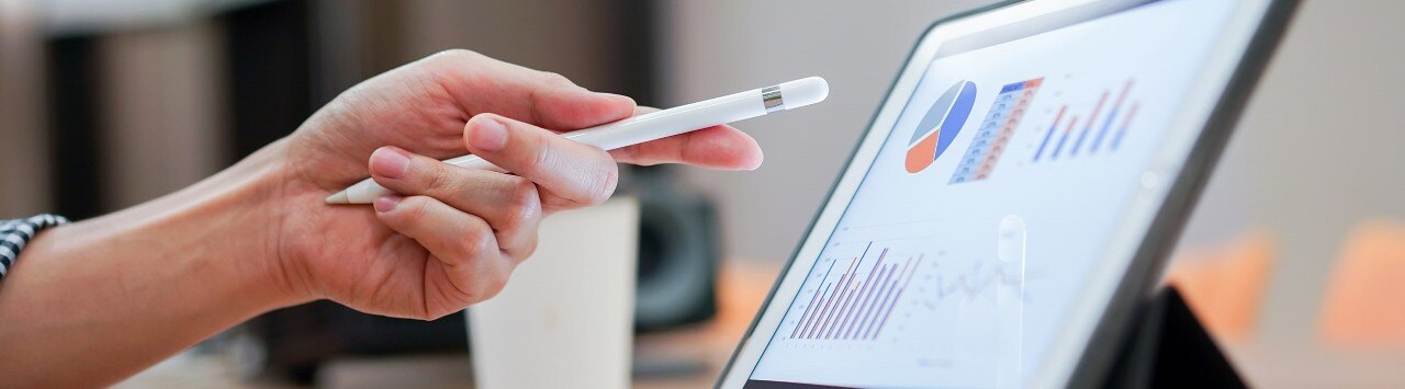A hand pointing a stylus at a tablet screen displaying graphs and charts
