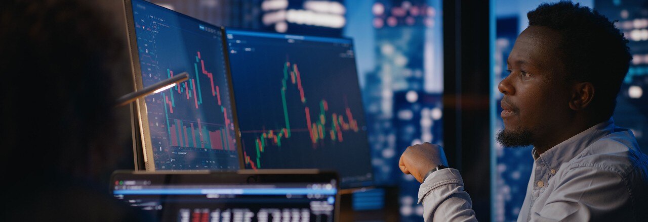 African-American financial analyst reviewing stock market data on two monitors