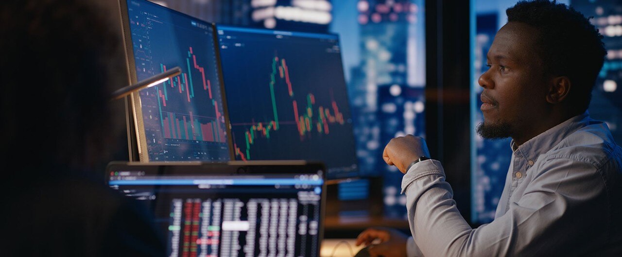 African-American financial analyst reviewing stock market data on two monitors