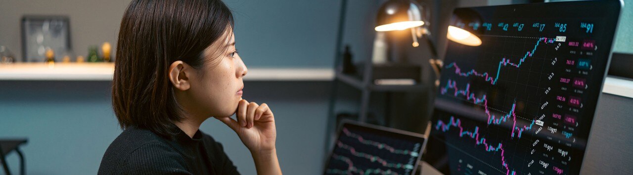 Asian-American female analyst reviewing stock market data on multiple monitors