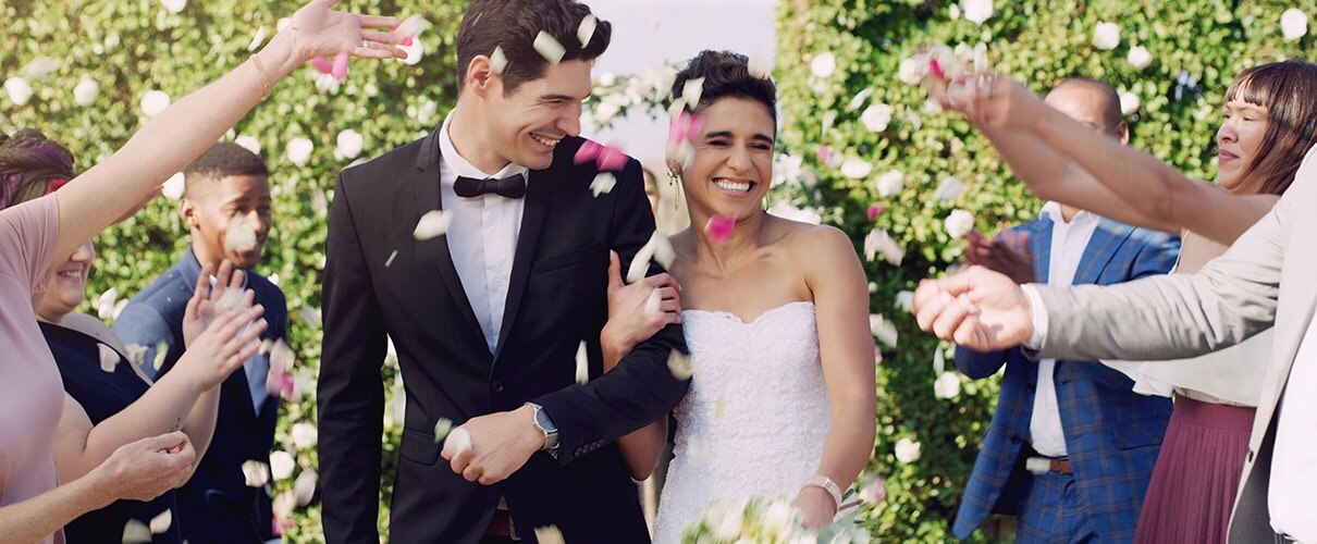 Smiling young newlyweds being showered with flower petals at wedding