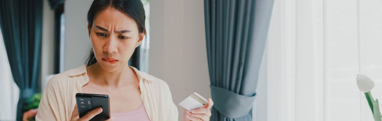 Asian-American woman with concerned expression looking at smartphone and holding credit card