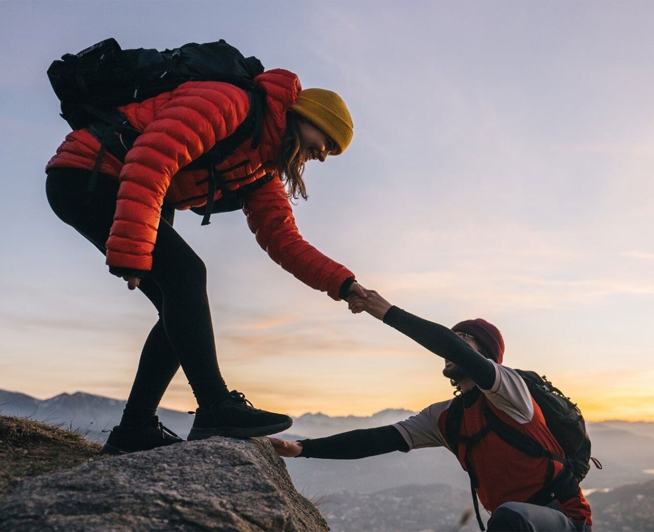 Woman offering man an outstretched hand as he climbs a mountain